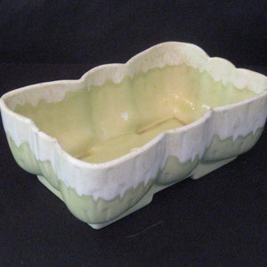 May include: A green and white ceramic planter with a wavy, scalloped edge. The planter is glazed in a light green colour with white accents.