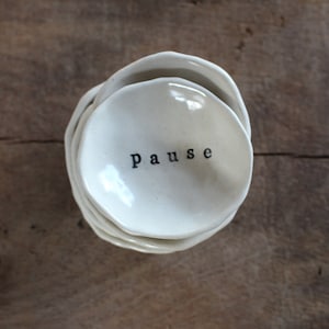 May include: A set of three white ceramic dishes stacked on top of each other. The top dish has the word "pause" written on it in black.
