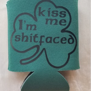 May include: Green neoprene can cooler with a black shamrock design. The shamrock has the text "Kiss me I'm shitfaced" on it.