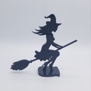 May include: Black silhouette of a witch riding a broomstick. The witch is wearing a pointed hat and a long dress. The broomstick is made of wood and has a long handle.