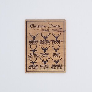 May include: A wooden sign with a Christmas dinner theme. The sign features reindeer silhouettes with names and food items associated with each reindeer. The text reads "Christmas Dinner" at the top of the sign.