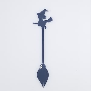 Op de afbeelding: Een zwarte metalen heksenroerlepeltje met een silhouet van een heks op een bezem.