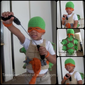 May include: A child wearing a green and orange crocheted Teenage Mutant Ninja Turtles costume. The costume includes a hat, mask, vest, and shell. The child is holding a black toy weapon.