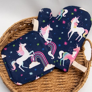 May include: A set of two blue and white unicorn-themed kitchen pot holders. One pot holder is a mitten style and the other is a square shape. Both pot holders feature a repeating pattern of unicorns, rainbows, and stars.