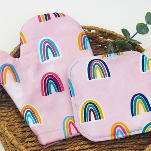 May include: A pink oven mitt and pot holder set with a rainbow pattern. The set is made of cotton and is perfect for protecting your hands from heat while cooking or baking.