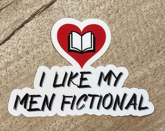 Könnte beinhalten: Ein weißer Aufkleber mit dem Text "I LIKE MY MEN FICTIONAL" in Schwarz, mit einem roten Herz und einer Buchgrafik. Der Aufkleber befindet sich auf einer Holzoberfläche.