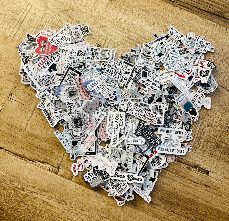 K&ouml;nnte beinhalten: Eine herzf&ouml;rmige Anordnung von &uuml;ber 100 Buch-Sticker. Die Sticker zeigen verschiedene Designs und Texte, darunter Zitate &uuml;ber B&uuml;cher, Kaffee und Lesen. Einige der Texte beinhalten "Book Nerd", "Book Lover", "Just mind ya business", "Who needs therapy when you have books", und "Books are cheaper than therapy".