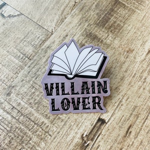 Op de afbeelding: Een zilveren sticker met een zwart-witte illustratie van een open boek en de tekst "VILLAIN LOVER" in zwart.