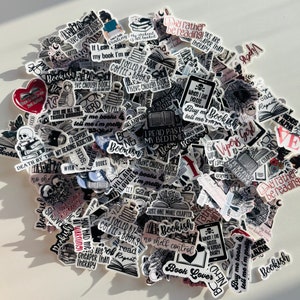 K&ouml;nnte beinhalten: Eine Sammlung von schwarz-wei&szlig;en Aufklebern mit roten und rosa Akzenten, die Buch-bezogene Zitate und Illustrationen zeigen. Die Aufkleber enthalten S&auml;tze wie "Ich w&uuml;rde lieber lesen", "Ich habe genug B&uuml;cher", "Bookish" und "Tod durch TBR".