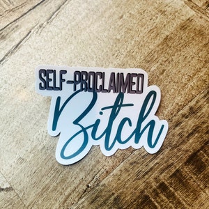 May include: A sticker with the text "SELF-PROCLAIMED Bitch" in a gradient teal and white design. The words are layered on a white background with a slight shadow effect, creating a 3D appearance. The sticker is placed on a wooden surface.