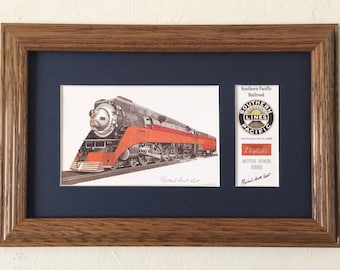 May include: A framed print of a Southern Pacific Railroad steam locomotive with the text "Daylight, Motive Power Series" and a logo of the Southern Pacific Railroad with the text "Southern Pacific Lines".