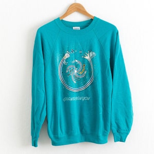 May include: Teal blue sweatshirt with a graphic print of a stylised Native American design with the text "Grand Canyon" below it.