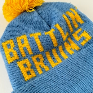 Könnte beinhalten: Blaue Strickmütze mit gelbem Bommel und der Aufschrift "Battlin' Bruins" in gelben Buchstaben.