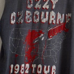 Puede incluir: Una camiseta gris sin mangas con un gr&aacute;fico blanco de la gira de Ozzy Osbourne de 1982. El gr&aacute;fico presenta un cuchillo ensangrentado y un mapa de los Estados Unidos.
