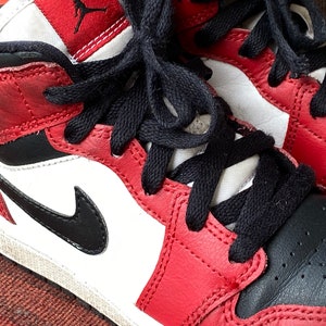 May include: Red, black, and white leather sneakers with black laces. The sneakers have a white midsole and a black outsole.