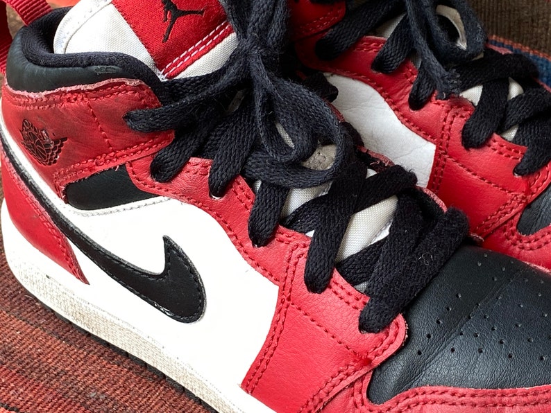 May include: Red, black, and white leather sneakers with black laces. The sneakers have a white midsole and a black outsole.