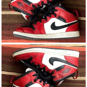 May include: A pair of red, white, and black sneakers with a black swoosh logo. The sneakers have a white midsole and a black outsole.