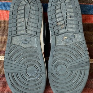 May include: A pair of black and white sneakers with red accents. The sneakers have a black sole with a circular pattern and the Nike logo on the back.