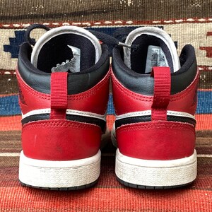 May include: A pair of red and black high-top sneakers with white soles. The sneakers have a black swoosh logo on the side and a white stripe above the sole.