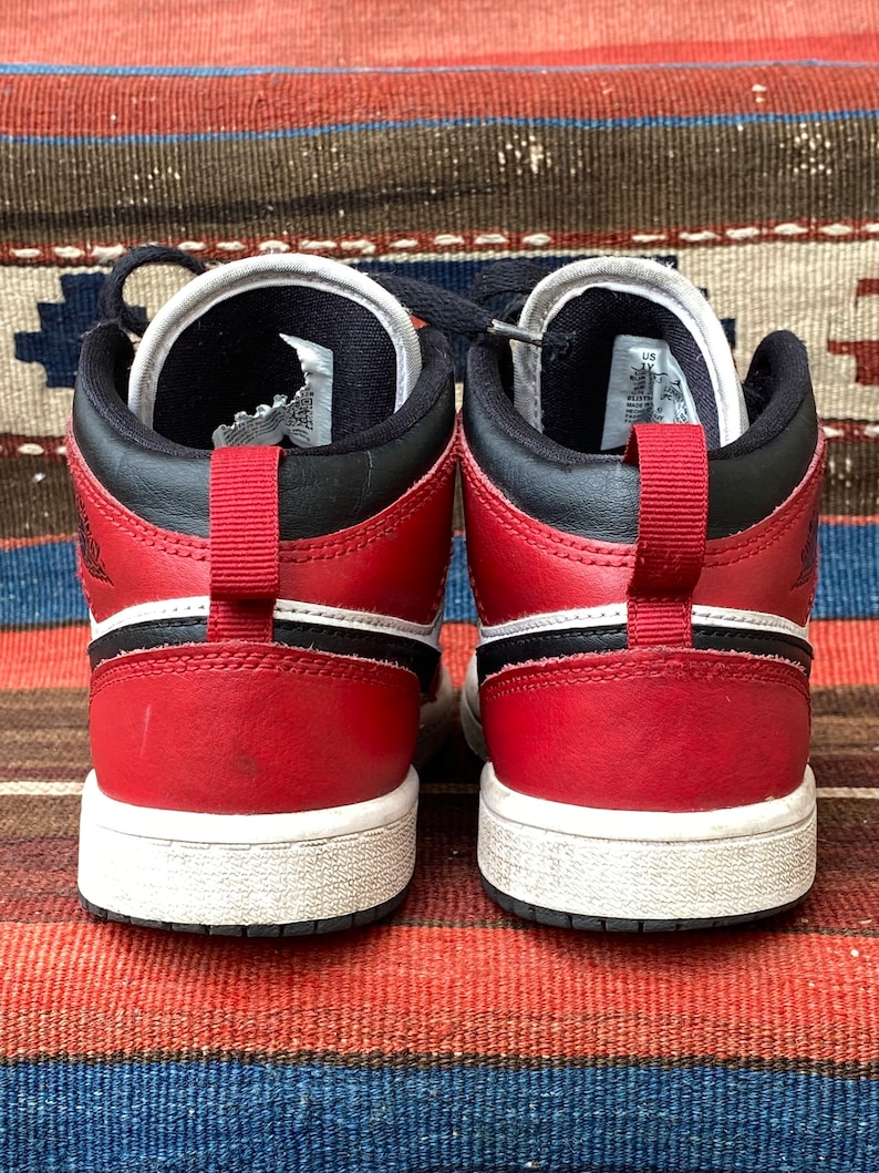 May include: A pair of red and black high-top sneakers with white soles. The sneakers have a black swoosh logo on the side and a white stripe above the sole.