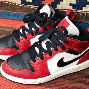 May include: Red and black leather sneakers with a white midsole and black laces. The sneakers have a Nike swoosh logo on the side.