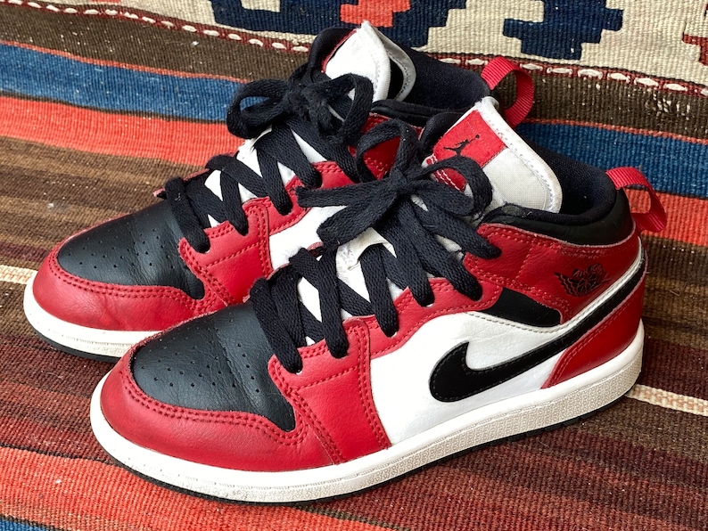 May include: Red and black leather sneakers with a white midsole and black laces. The sneakers have a Nike swoosh logo on the side.