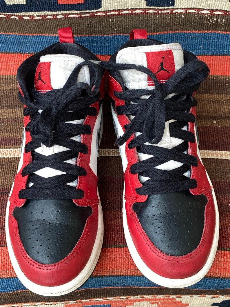 May include: A pair of red and black sneakers with white accents. The sneakers have black laces and a white midsole.