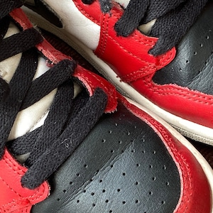 May include: Close-up of a pair of red and black sneakers with white accents. The shoes have black laces and a white midsole.