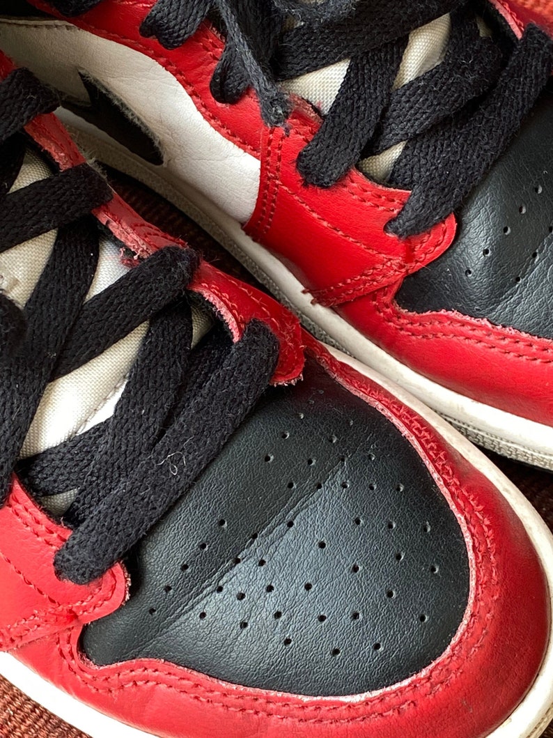 May include: Close-up of a pair of red and black sneakers with white accents. The shoes have black laces and a white midsole.