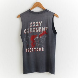 Puede incluir: Camiseta gris sin mangas con un gr&aacute;fico descolorido rojo y blanco de un mapa de los Estados Unidos con un cuchillo atraves&aacute;ndolo. El texto "Ozzy Osbourne 1982 Tour" est&aacute; impreso debajo del gr&aacute;fico.