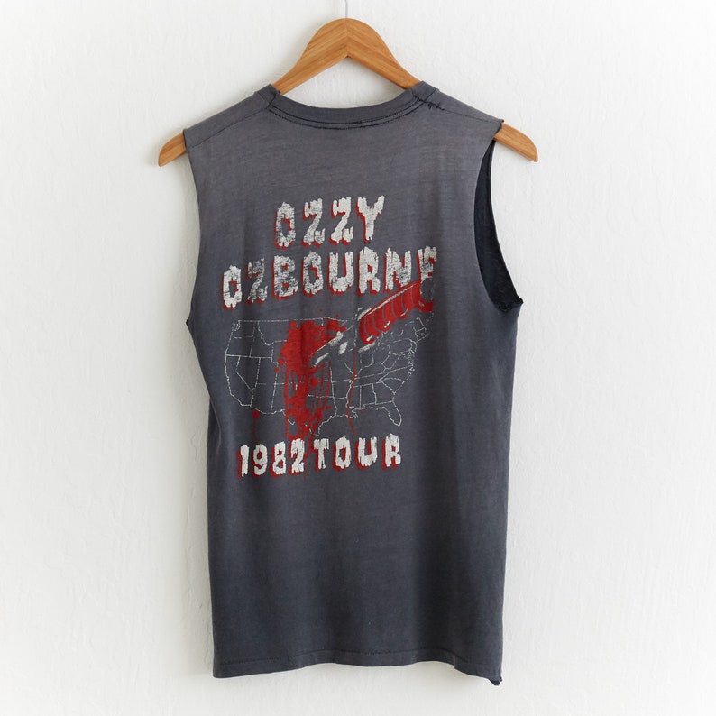 Puede incluir: Camiseta gris sin mangas con un gr&aacute;fico descolorido rojo y blanco de un mapa de los Estados Unidos con un cuchillo atraves&aacute;ndolo. El texto "Ozzy Osbourne 1982 Tour" est&aacute; impreso debajo del gr&aacute;fico.