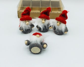 May include: Four small gnome figurines with red knit hats, gray knit sweaters, and long white beards. The gnomes have wooden noses and arms. A clear plastic and cardboard box is in the background.