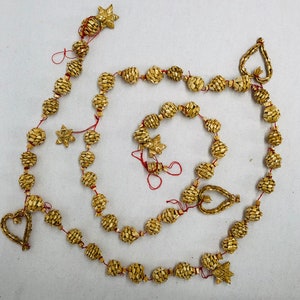 May include: A decorative garland featuring woven straw spheres, stars, and heart shapes, strung together with red thread. The garland is a natural beige color and is suitable for holiday or seasonal decor.