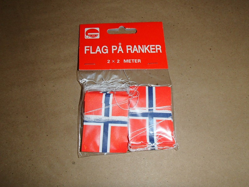May include: A package of Norwegian flag banners. The flags are red with a blue cross outlined in white, and are strung on white string. The package is red with the text "FLAG P&Aring; RANKER" and "2 x 2 METER".