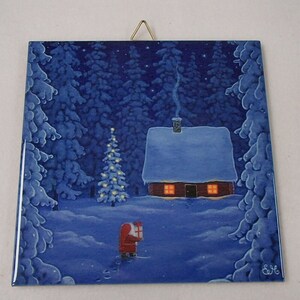May include: A square ceramic wall tile featuring a winter scene with a snow-covered cabin, a lit Christmas tree, and a figure in a red suit carrying a gift. The dark blue forest background is filled with snow-laden pine trees and a starry night sky.