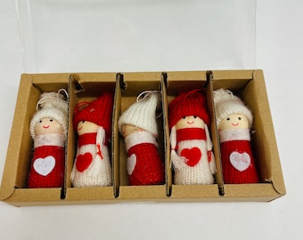 May include: A set of five handmade Christmas ornaments. Each ornament is a small doll with a wooden head, a red and white knitted body, and a heart-shaped detail. The dolls are packaged in a cardboard box with individual compartments.