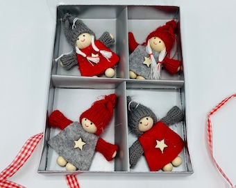 May include: A set of four decorative dolls in a silver box. Each doll has a wooden head, gray knitted arms, and a red or gray felt body. The dolls wear knitted hats and have a wooden star or white tassel. A red and white checkered ribbon is visible.