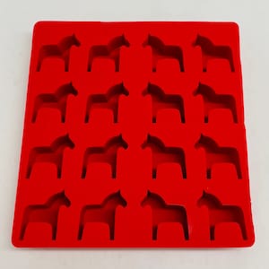 May include: A bright red silicone mold featuring a grid of sixteen Dala horse shapes. The mold is square and the horse shapes are evenly spaced, creating a repeating pattern. The design is simple and the color is vibrant.