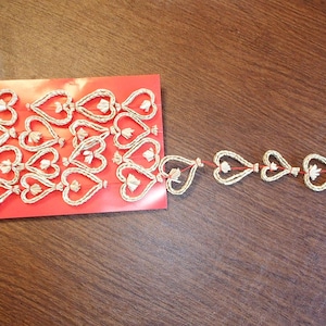 May include: A collection of woven heart-shaped ornaments with floral accents. The hearts are arranged on a red card and strung together on a red string. The ornaments are made of a light-colored, natural material.