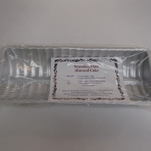 May include: A rectangular, fluted aluminum baking pan, wrapped in clear plastic. A label on the pan reads "Scandinavian Almond Cake" with a recipe. The pan is designed for baking cakes and other desserts.