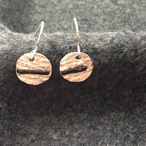 May include: A pair of silver earrings with black accents. The earrings are round and have a textured surface.