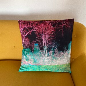 May include: A throw pillow featuring an abstract design of trees and a building in the background. The pillow is on a yellow sofa.