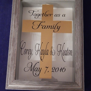 Könnte beinhalten: Eine gerahmte Schattenbox mit einem goldenen Kreuz und dem Text "Together as a Family Corey, Kayla & Keaton May 7, 2016".