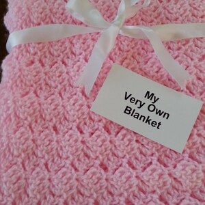 May include: A pink crocheted baby blanket with a white ribbon tied in a bow. The blanket has a tag that says "My Very Own Blanket".