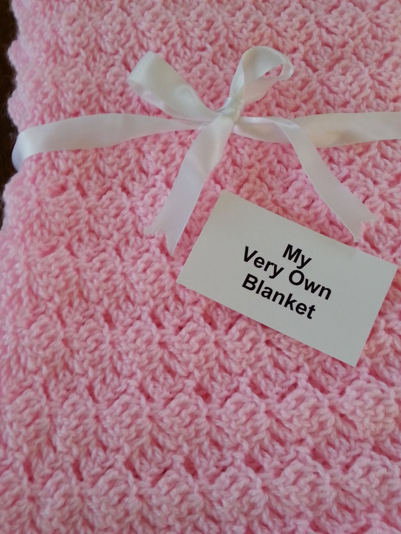 May include: A pink crocheted baby blanket with a white ribbon tied in a bow. The blanket has a tag that says "My Very Own Blanket".