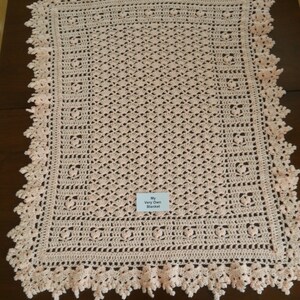 Puede incluir: Una manta de beb&eacute; de ganchillo en color rosa p&aacute;lido con un delicado borde de encaje. La manta tiene una etiqueta que dice "My Very Own Blanket".