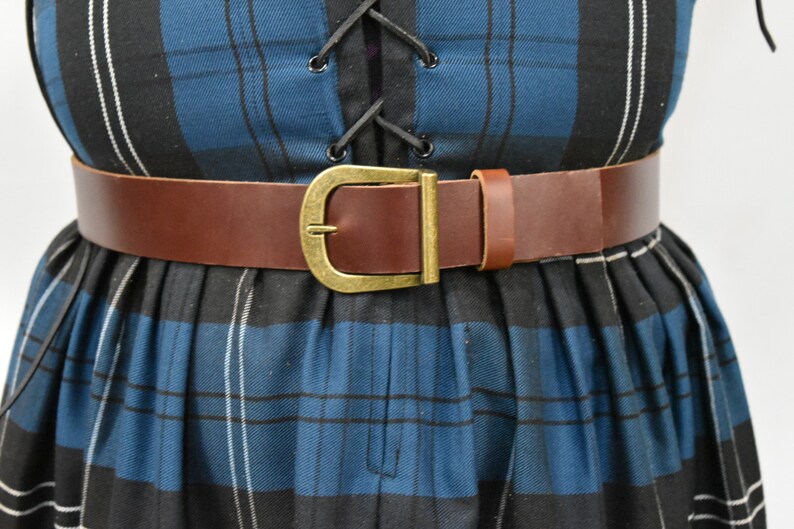 May include: A brown leather belt with a brass buckle. The belt is worn over a blue and black plaid dress.
