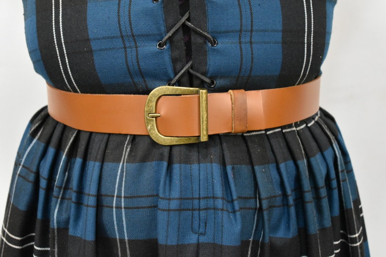 May include: A brown leather belt with a gold-toned buckle. The belt is worn over a blue and black plaid dress.