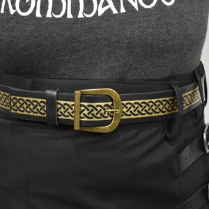 May include: A black leather belt with a gold Celtic knot design. The belt has a brass buckle.