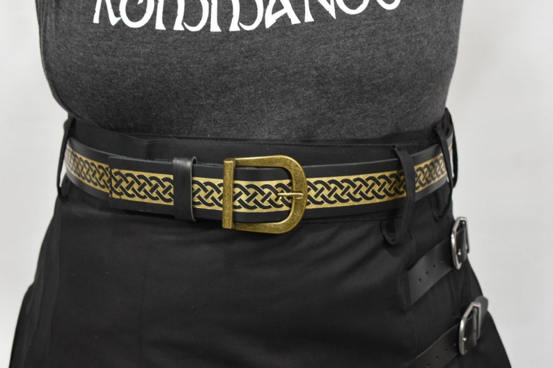 May include: A black leather belt with a gold Celtic knot design. The belt has a brass buckle.